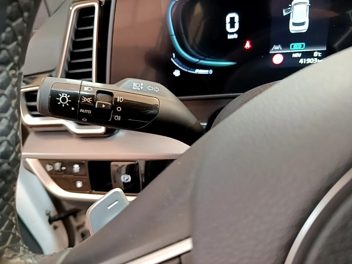 Gros plan sur la manette des feux et le tableau de bord numérique du Kia Sportage blanc, affichage digital visible.