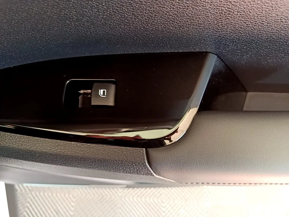 Gros plan sur le bouton de commande de la vitre électrique côté conducteur, intérieur noir et gris du Kia Sportage blanc.