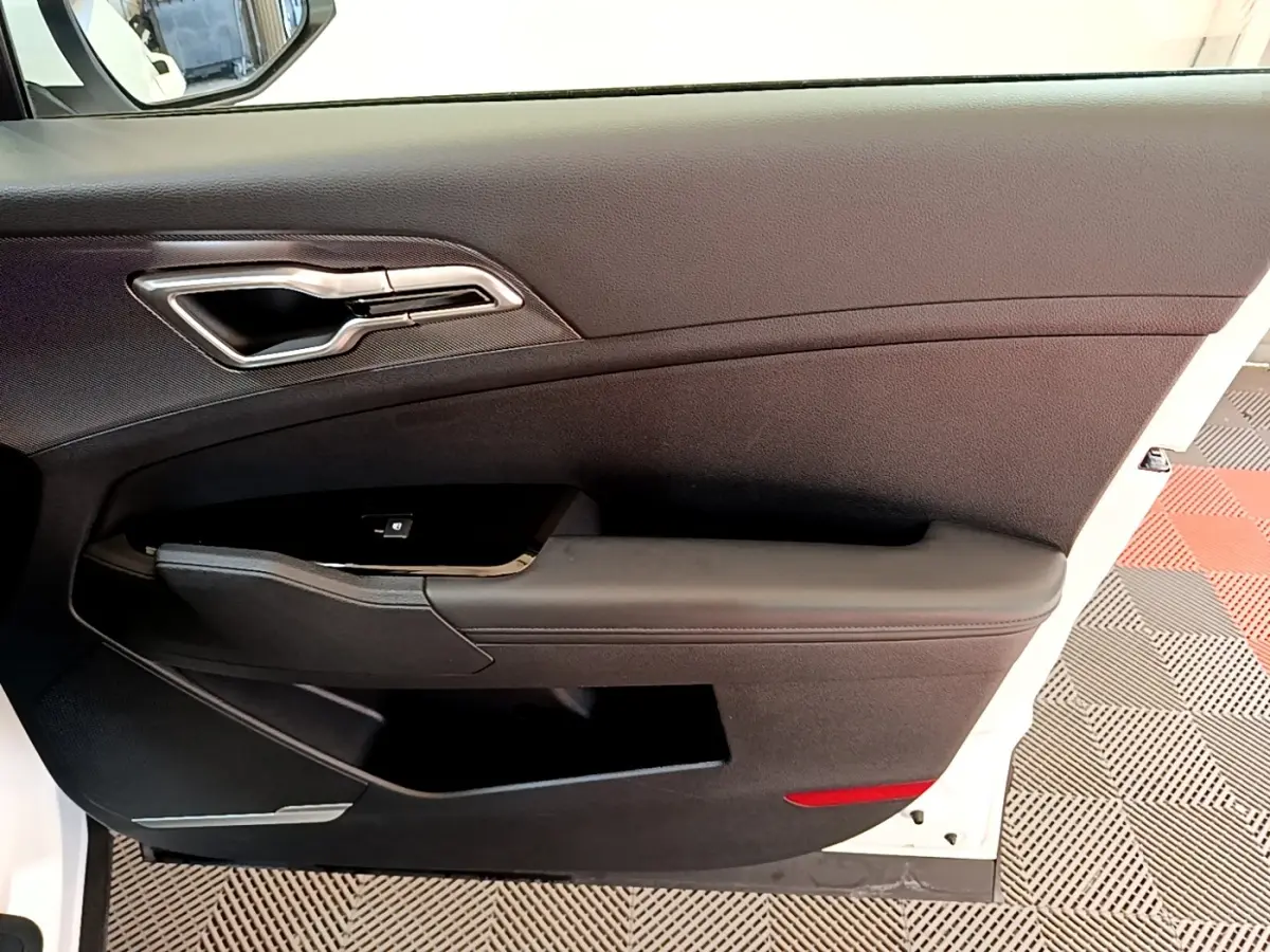 Vue intérieure côté gauche de la porte avant noire d’un Kia Sportage blanc avec poignée argentée et commande de fenêtre.