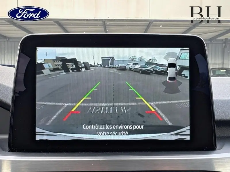 Écran tactile affichant la caméra de recul du Ford Kuga blanc Glacier, vue arrière avec lignes de guidage colorées.