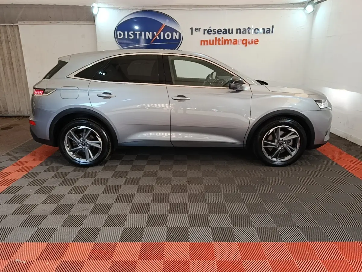 Vue de profil côté gauche d’un DS7 Crossback E-TENSE 225 Business gris foncé en intérieur sur sol damier noir et rouge.