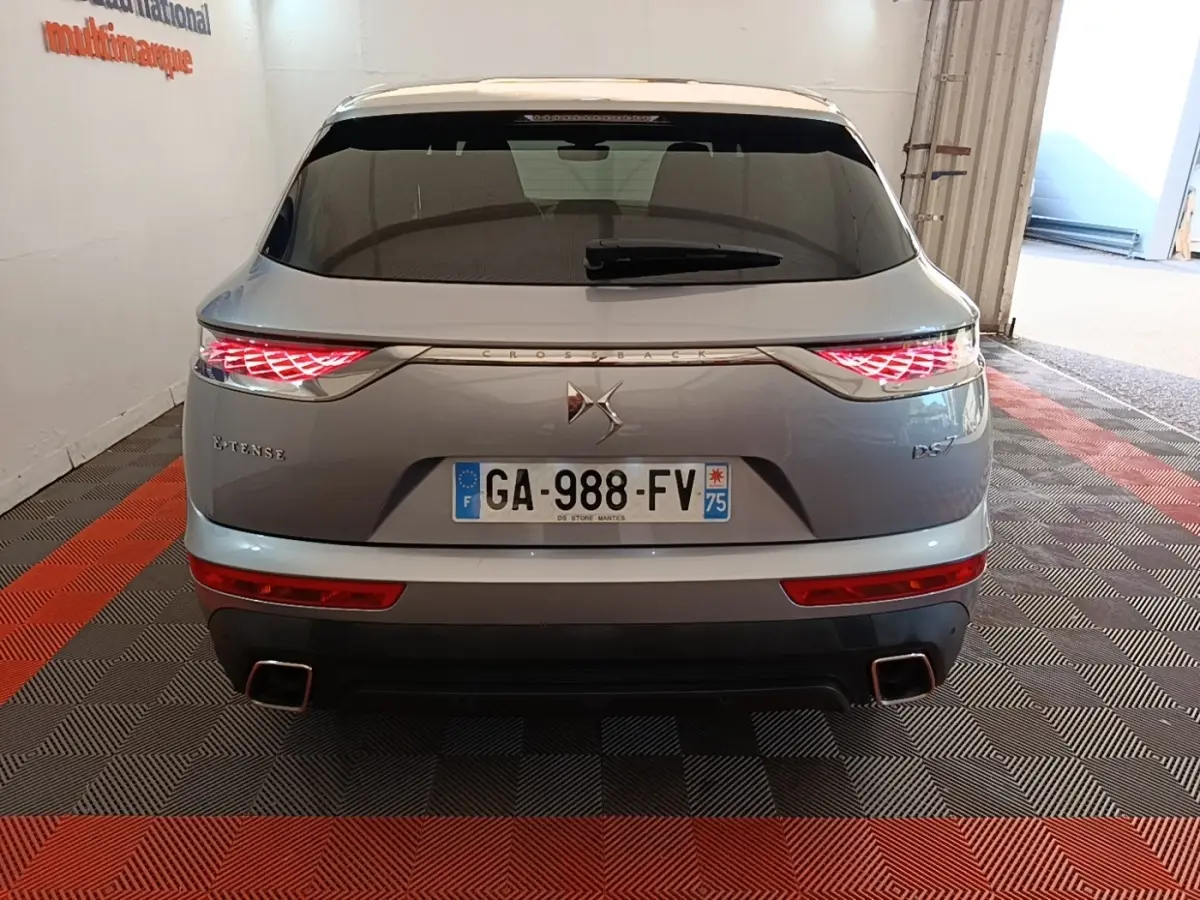 Vue arrière d’un DS7 Crossback E-TENSE gris foncé avec feux arrière LED allumés et double sortie d’échappement carrée.