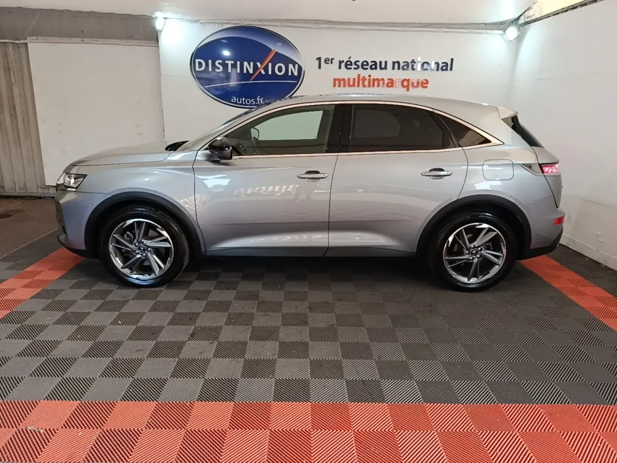 Vue latérale droite d’un DS7 Crossback gris foncé avec jantes alliage et feux arrière LED allumés en intérieur showroom.