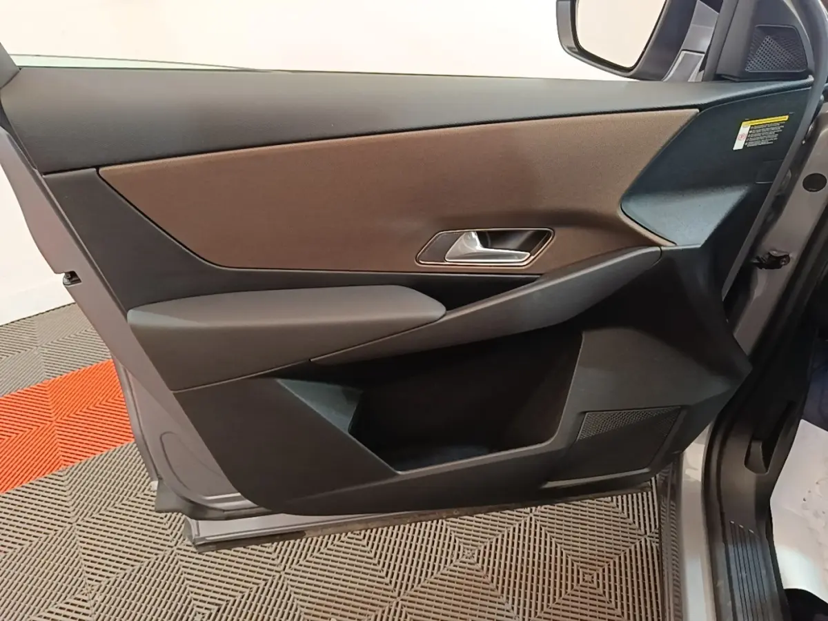 Vue rapprochée de la porte avant droite du DS7 Crossback gris foncé, avec garniture marron et poignée argentée.