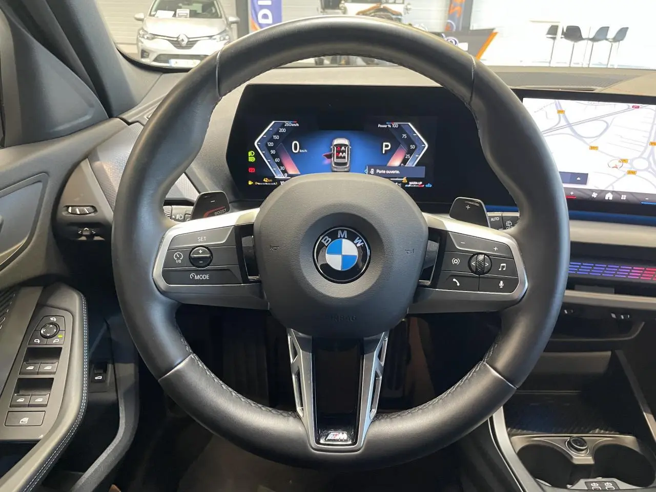 Vue intérieure centrée sur le volant cuir noir M Sport et le tableau de bord numérique de la BMW Série 1 120d gris.