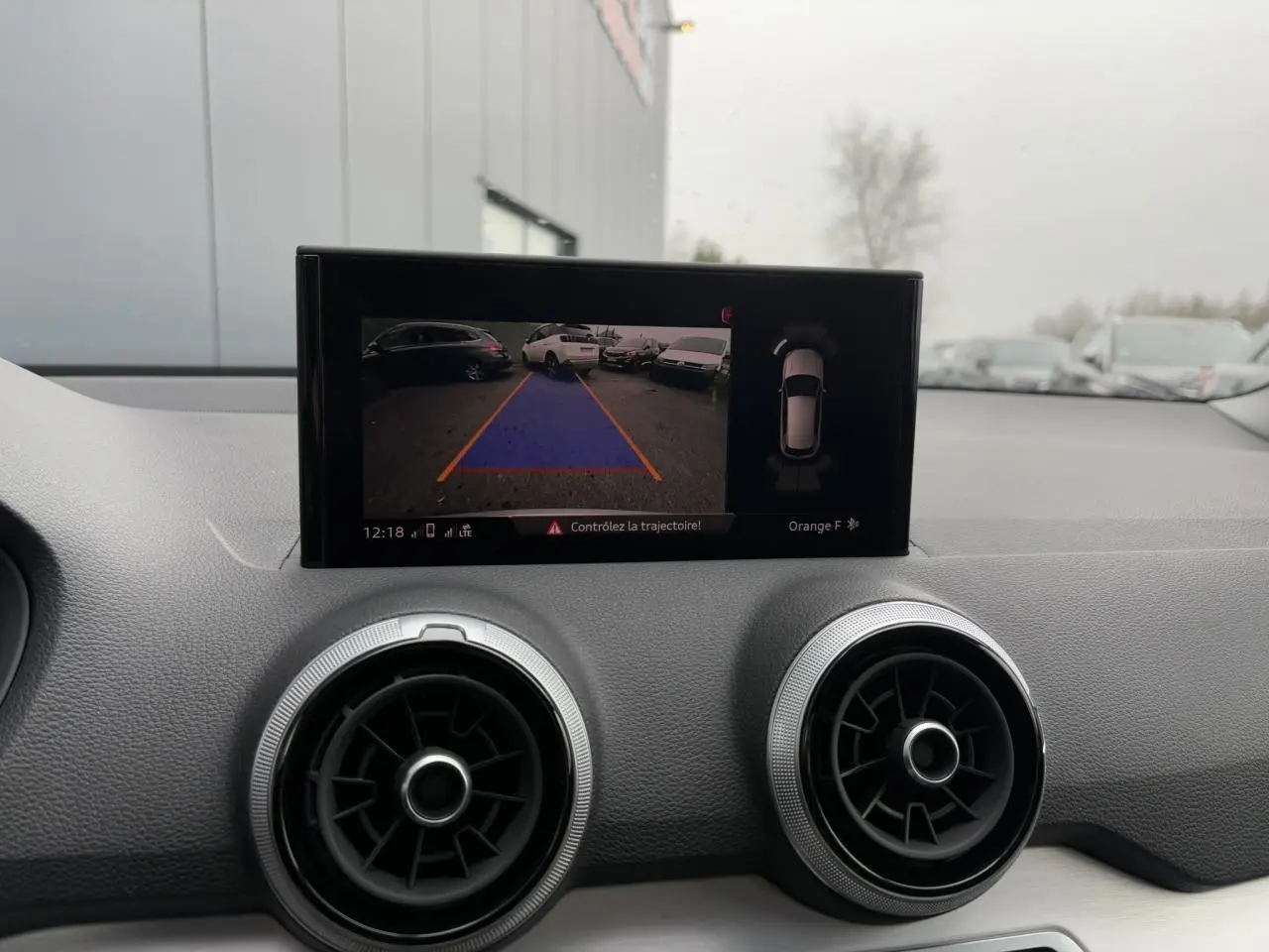 Vue intérieure du tableau de bord de l'Audi Q2 blanc Glacier 2024, écran affichant la caméra de recul et l'aide au stationnement.
