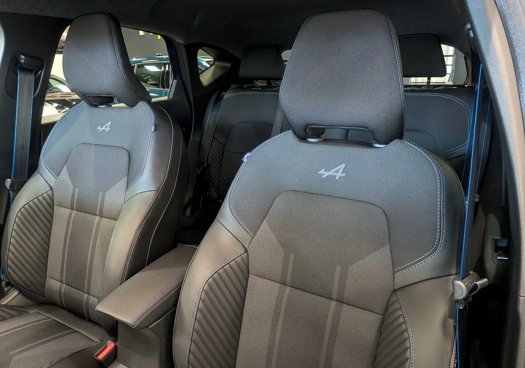 Gros plan sur les sièges avant noirs avec surpiqûres bleues et logo Alpine du Renault Captur E-TECH 2025.