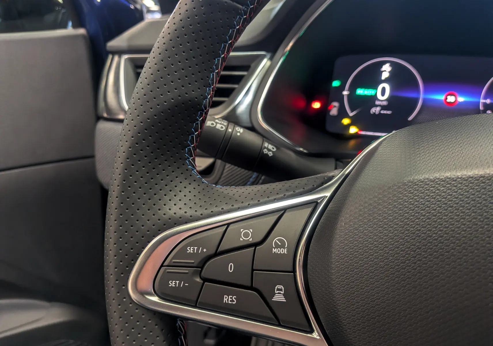 Gros plan sur le volant cuir perforé du Renault Captur E-TECH 2025 avec commandes de régulateur et tableau de bord numérique.