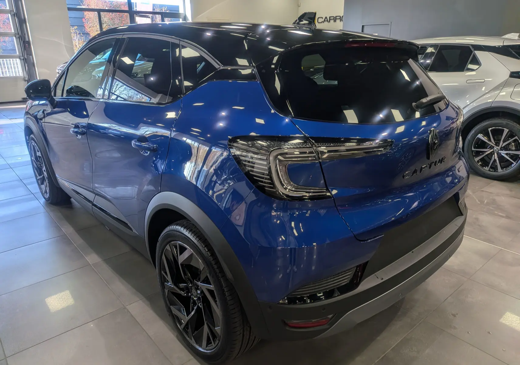 Vue 3/4 arrière droite du Renault Captur E-TECH bleu Iron avec toit noir et jantes noires en showroom.