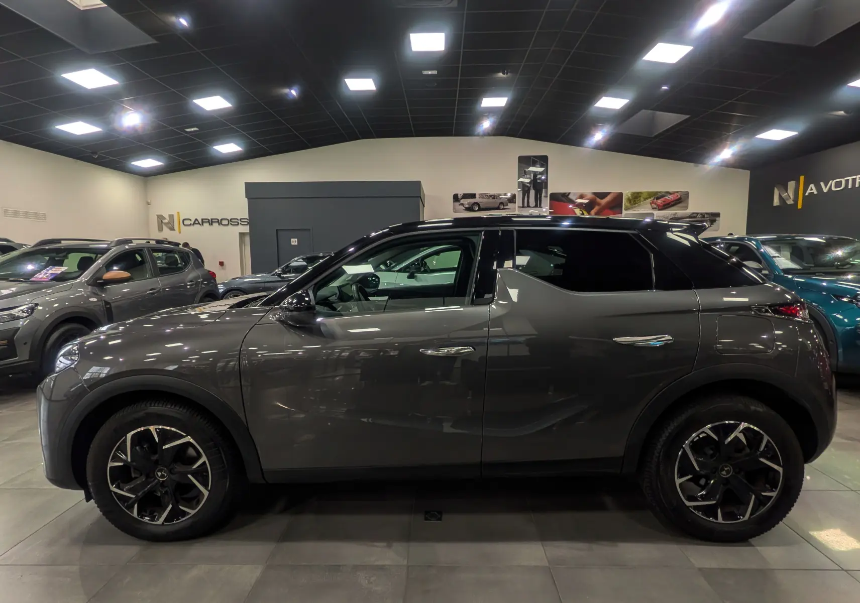 Vue de profil côté gauche du DS3 Crossback gris Platinium avec toit noir dans un showroom lumineux.