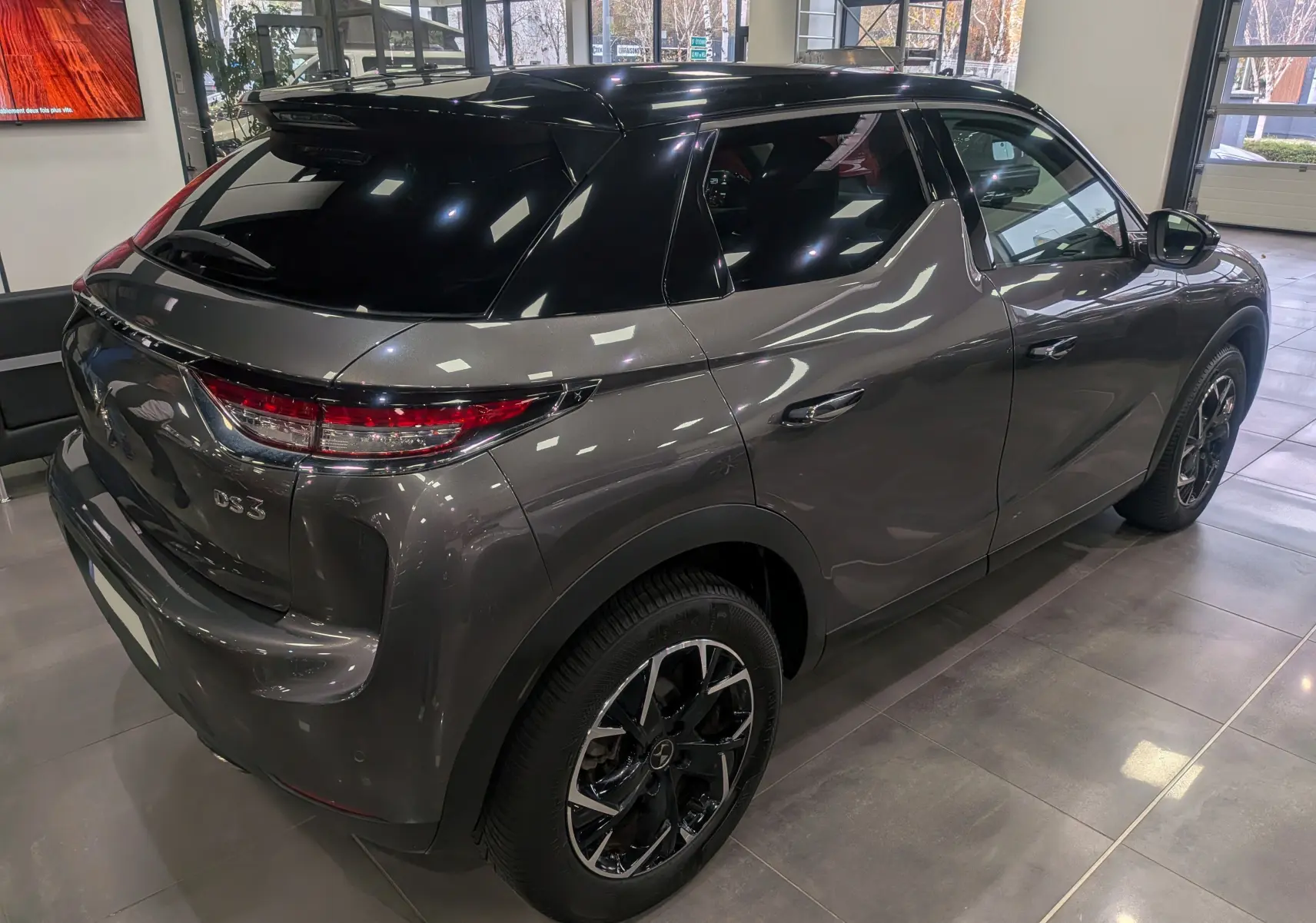 Vue 3/4 arrière droite du DS3 Crossback gris Platinium avec toit noir et jantes noires en showroom.