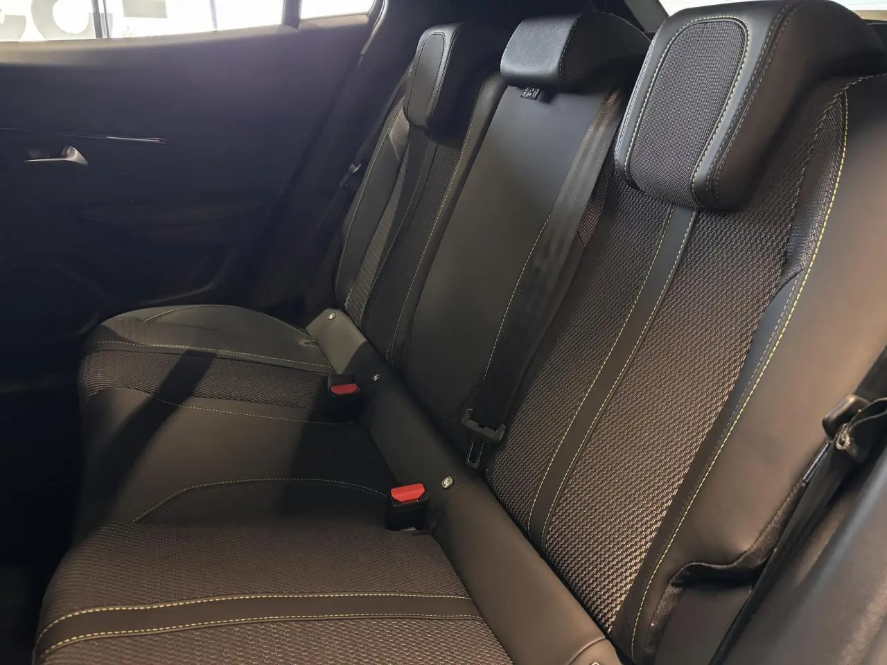 Vue latérale intérieure des sièges arrière noirs avec surpiqûres jaunes du Peugeot 2008 hybride blanc 2025.
