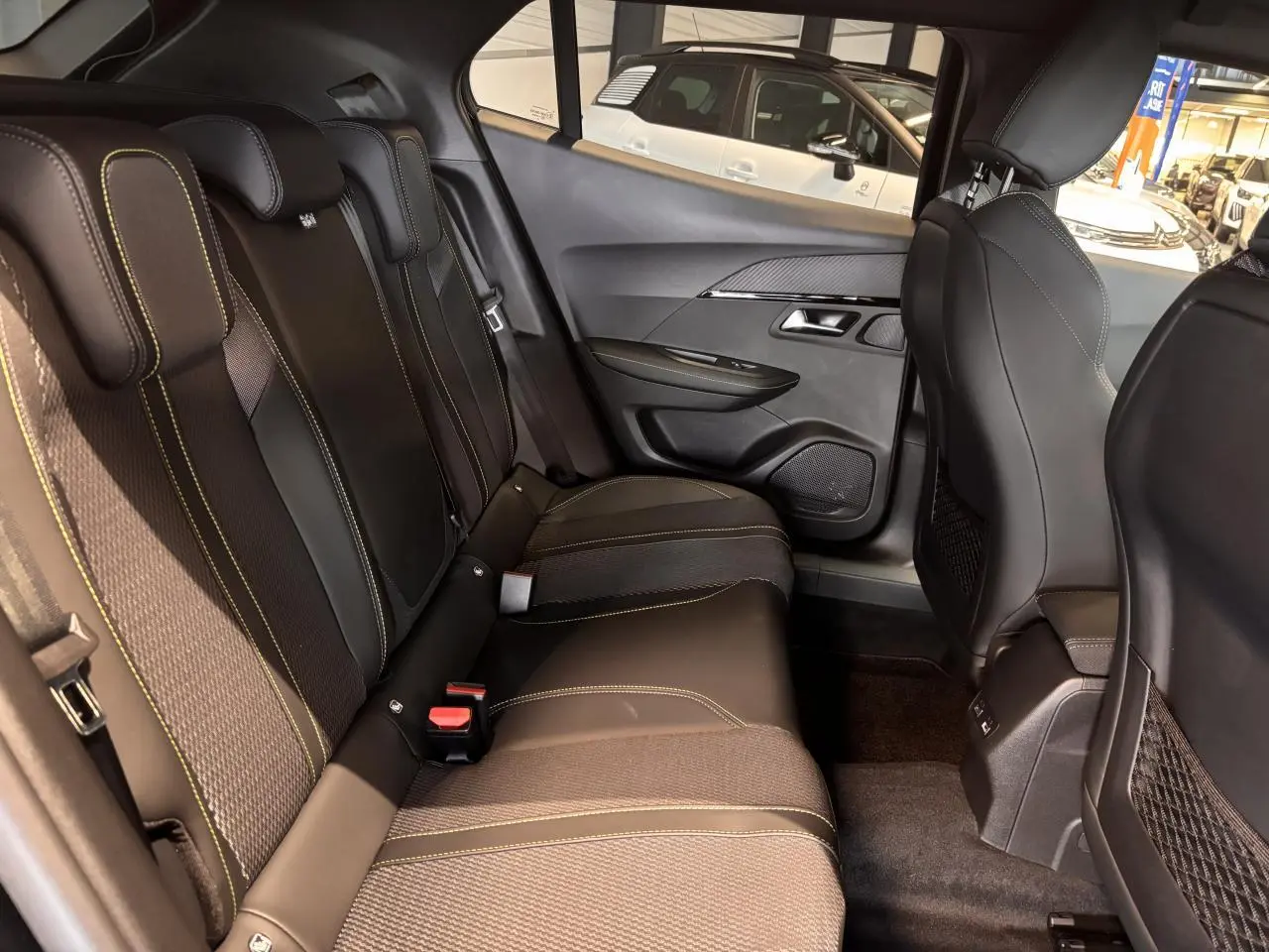 Vue intérieure arrière droite du Peugeot 2008 blanc, montrant les sièges arrière en tissu et cuir avec surpiqûres jaunes.