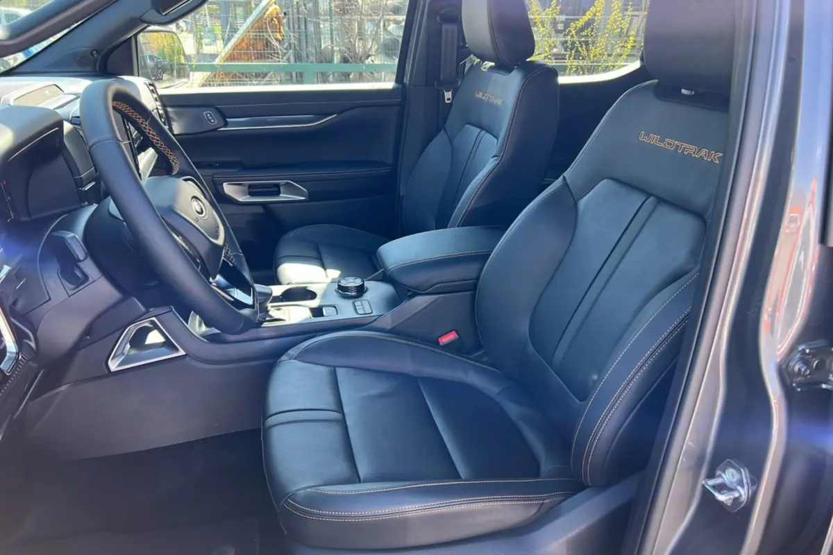 Intérieur côté conducteur du Ford Ranger Wildtrak gris carbone, sièges cuir noirs avec surpiqûres orange et logo Wildtrak brodé.