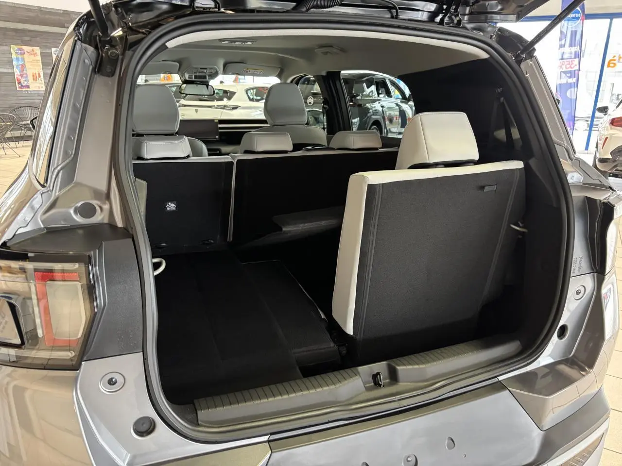 Coffre ouvert vue arrière d’un Citroën C3 Aircross gris avec banquette arrière rabattue et sièges blancs visibles.