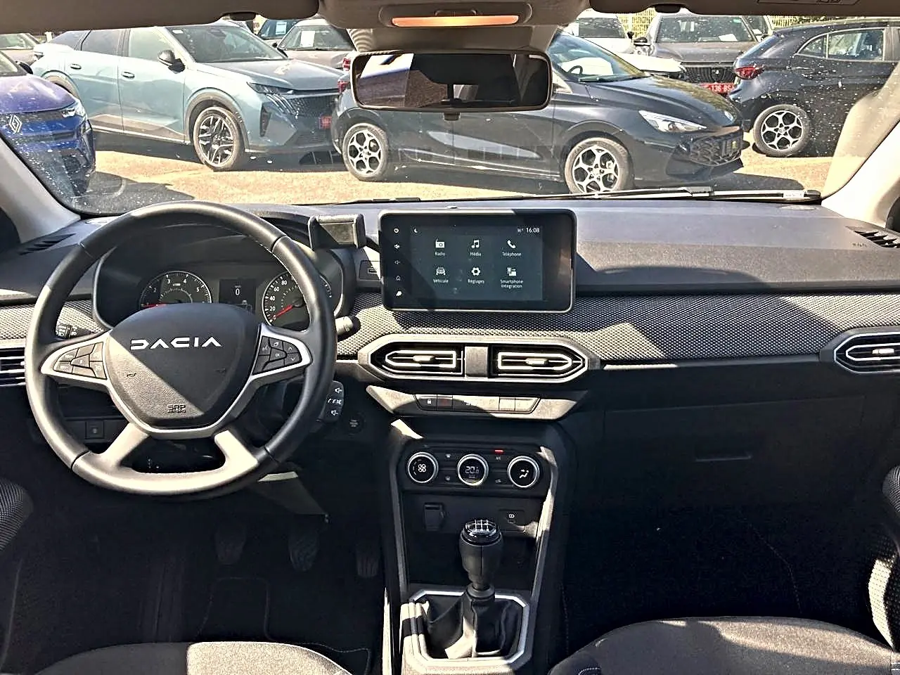 Vue intérieure avant du tableau de bord noir de la Dacia Sandero 2025 avec volant multifonctions et écran tactile central.