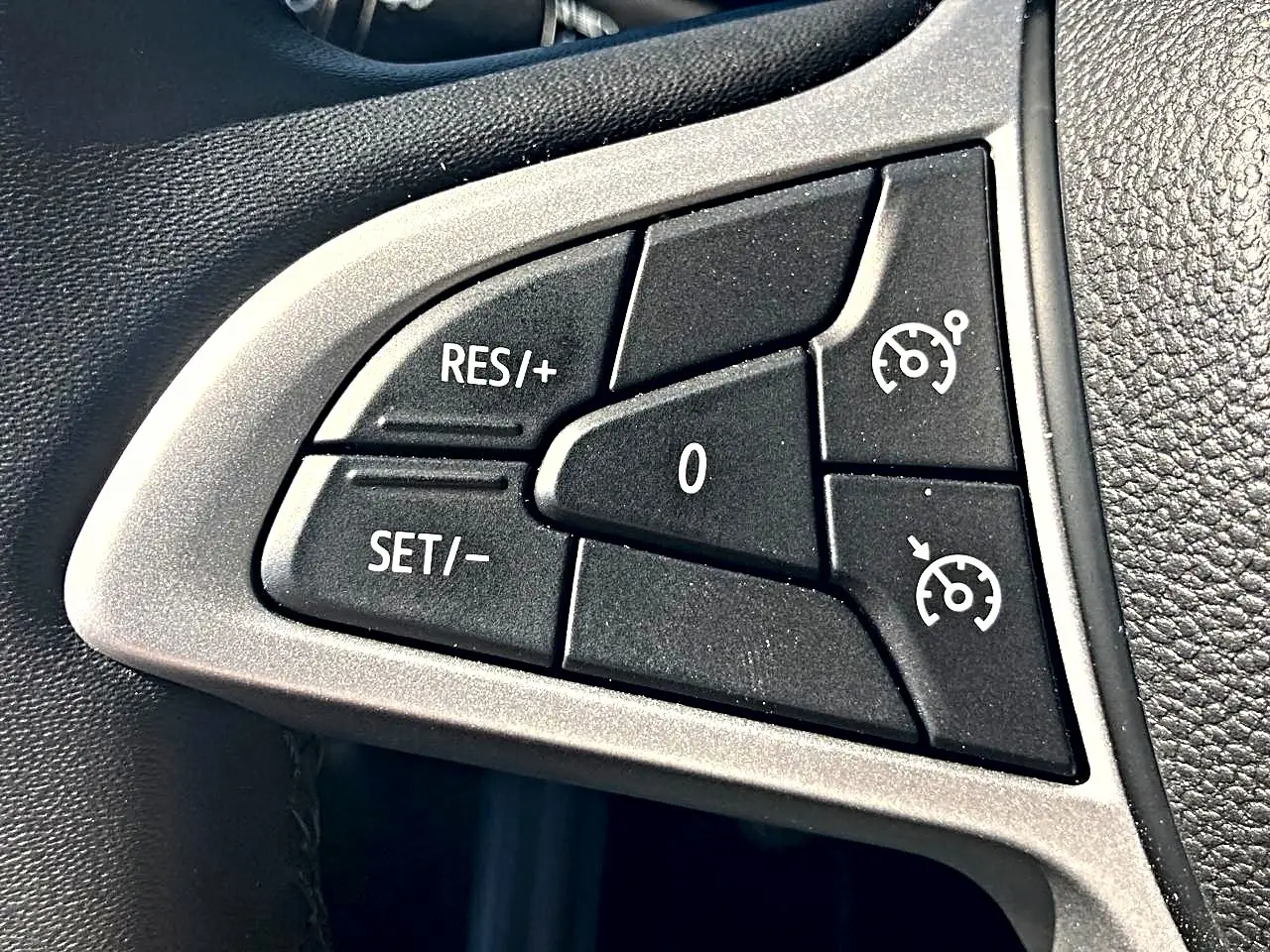 Gros plan sur les commandes noires du régulateur de vitesse sur le volant gris et noir d’une Dacia Sandero blanche.