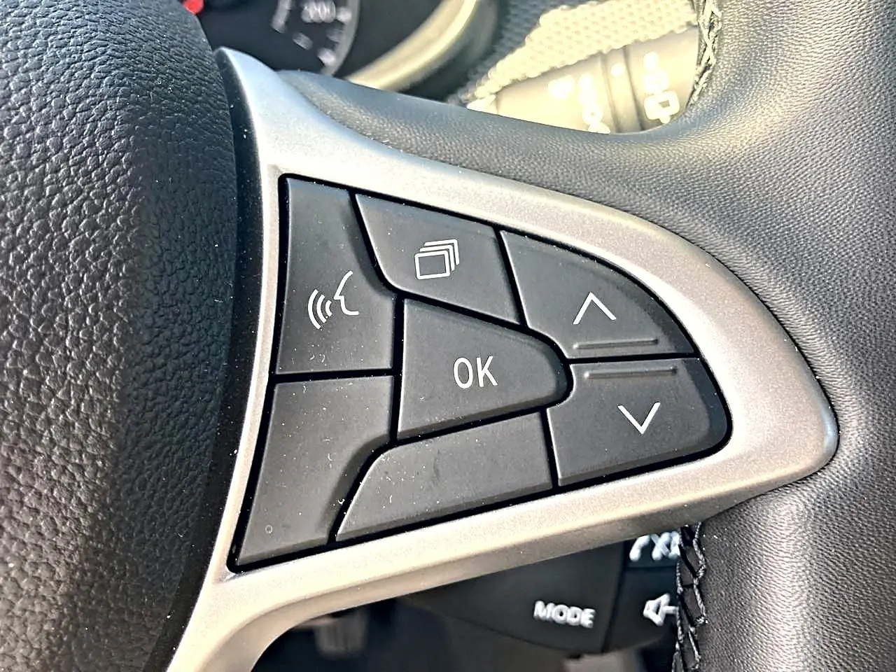 Gros plan sur les commandes noires du volant de la Dacia Sandero blanche, avec boutons directionnels et OK.