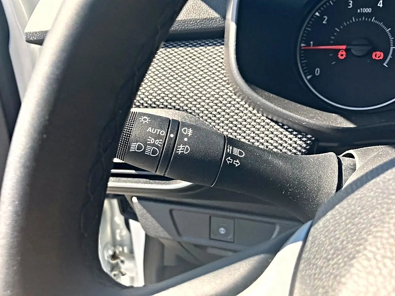 Gros plan sur la commande des feux et clignotants à gauche du volant dans l’habitacle d’une Dacia Sandero blanche.