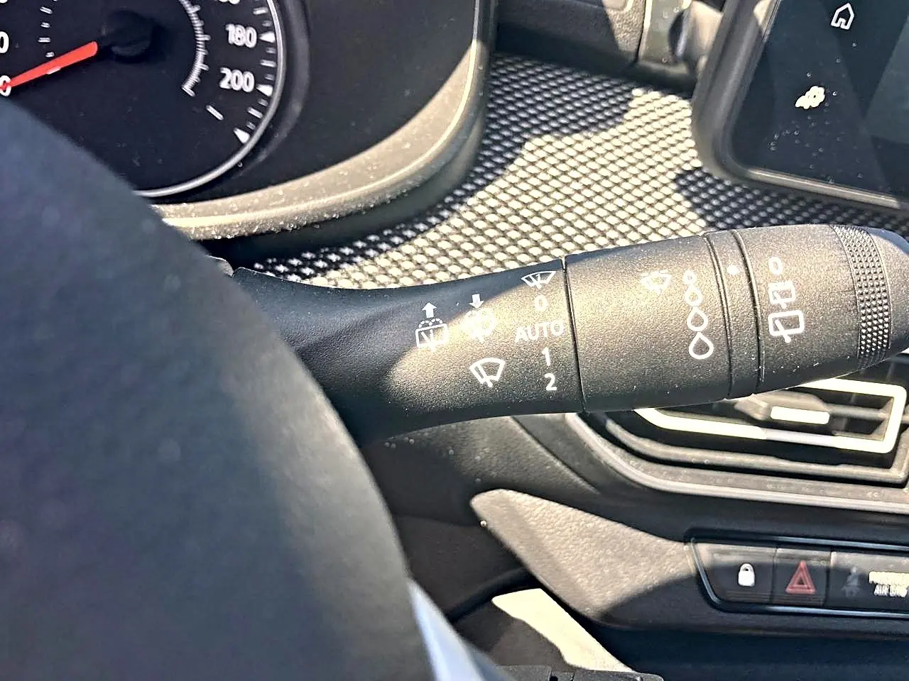 Gros plan sur la commande d’essuie-glace à gauche du volant dans l’habitacle noir d’une Dacia Sandero blanche 2025.