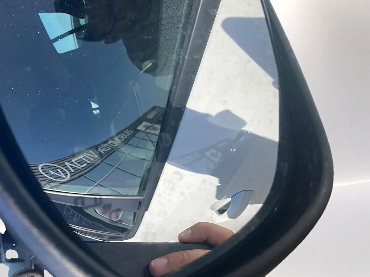 Rétroviseur côté droit montrant une Dacia Sandero blanche avec reflet d’un bâtiment et main sur la portière.