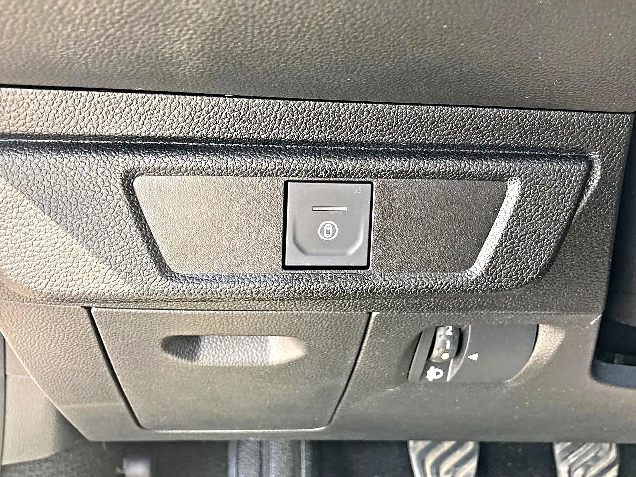 Gros plan sur le bouton de verrouillage centralisé noir sur le tableau de bord noir de la Dacia Sandero blanche.