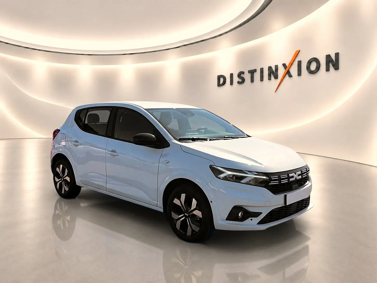 Dacia Sandero blanc vue 3/4 avant droit en intérieur avec jantes alu et calandre noire distinctive.