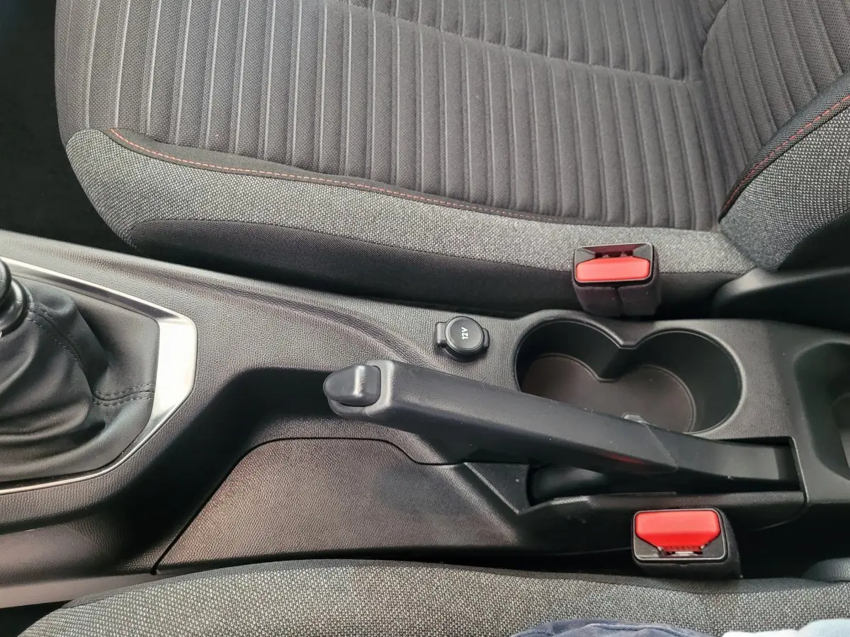 Vue rapprochée de la console centrale et frein à main d'une Peugeot 208 gris foncé avec sièges tissu gris et coutures rouges.