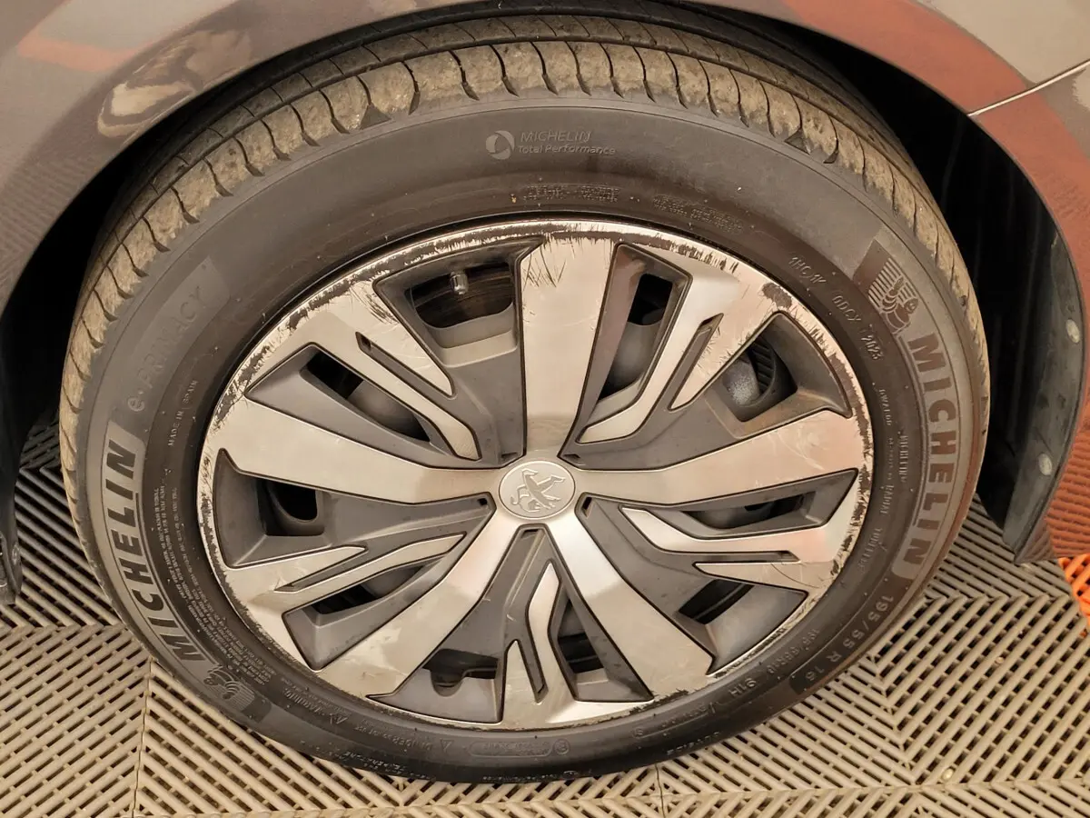 Gros plan sur la roue avant gauche d'une Peugeot 208 gris foncé avec jante en alliage au design moderne.