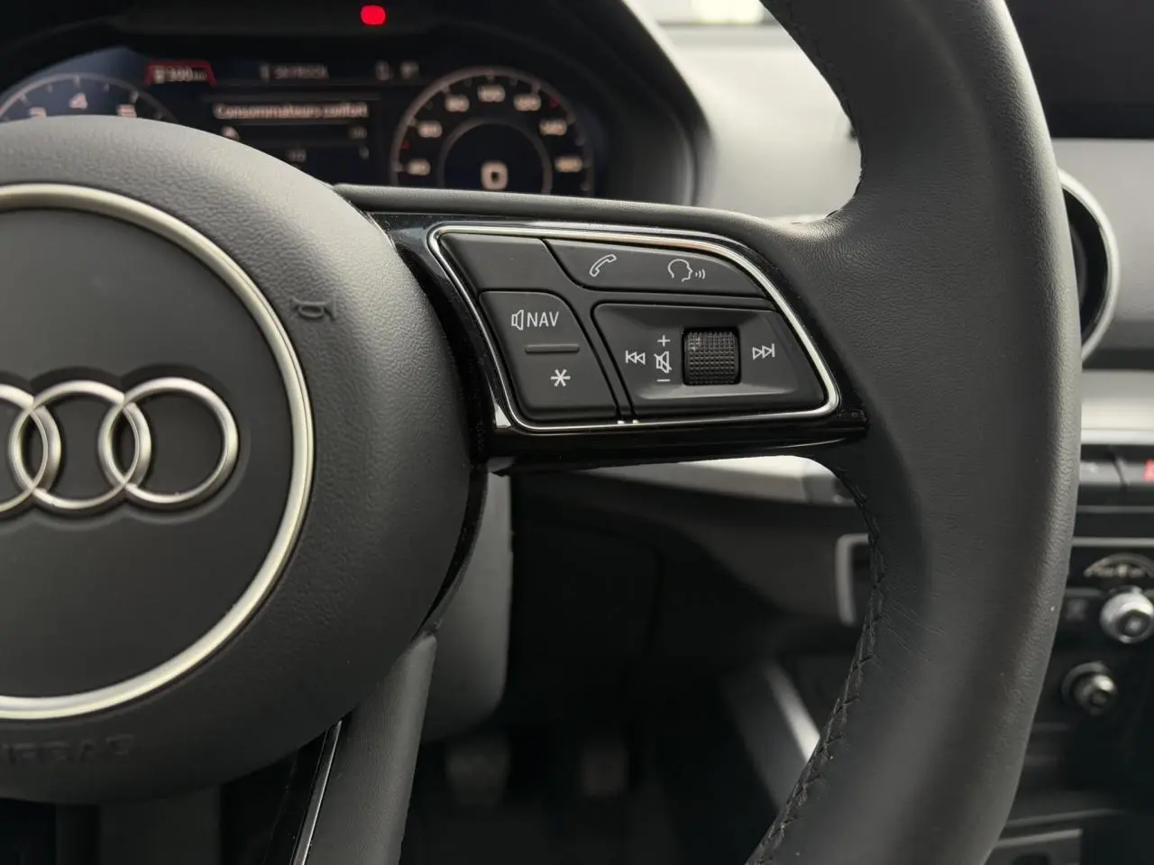 Gros plan sur le volant cuir noir de l'Audi Q2 30 TFSI 110 S-Line 2024 avec commandes multifonctions et tableau de bord numérique flou.