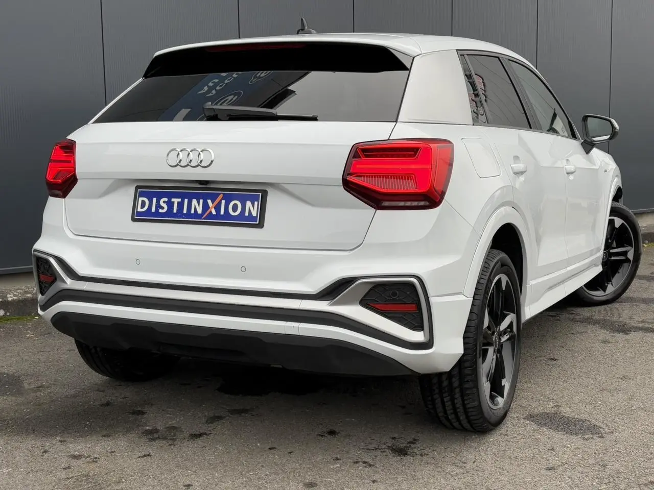 Audi Q2 30 TFSI S-Line blanc Glacier en 3/4 arrière droit avec jantes noires et feux arrière LED distinctifs.