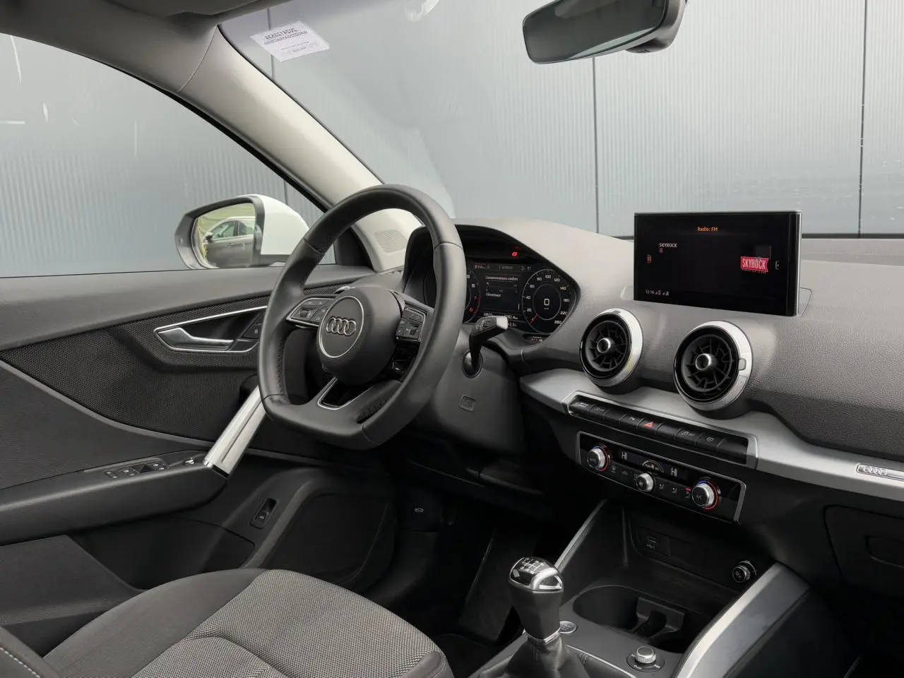Vue intérieure côté conducteur de l'Audi Q2 30 TFSI S-Line 2024 avec tableau de bord noir et écran central.