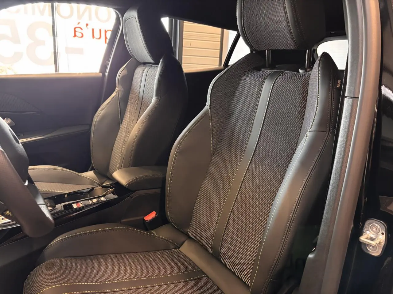 Vue rapprochée des sièges avant en cuir noir et tissu gris avec surpiqûres jaunes du Peugeot 2008 gris hybride 2025.