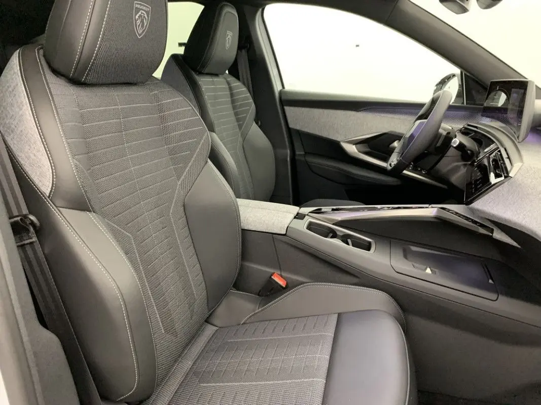 Vue intérieure côté gauche du Peugeot 3008 Hybrid 2026, sièges gris avec logo Peugeot brodé sur les appuie-têtes.
