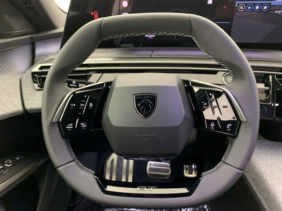 Vue rapprochée du volant gris perforé du Peugeot 3008 Hybrid 2026 avec logo central et commandes tactiles intégrées.