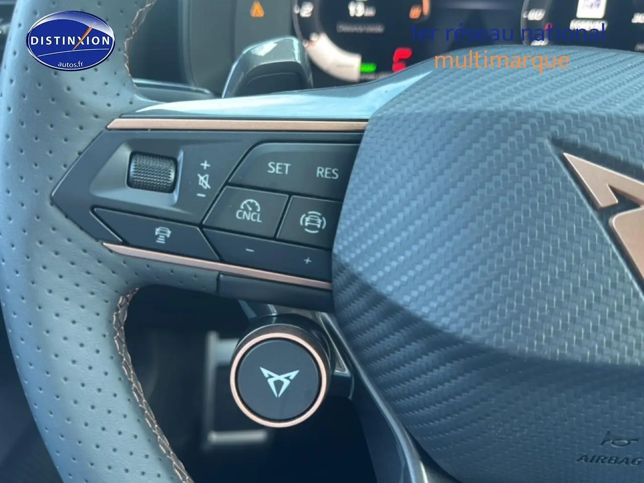 Gros plan sur le volant sport en cuir perforé avec commandes multifonctions et logo CUPRA sur fond carbone.