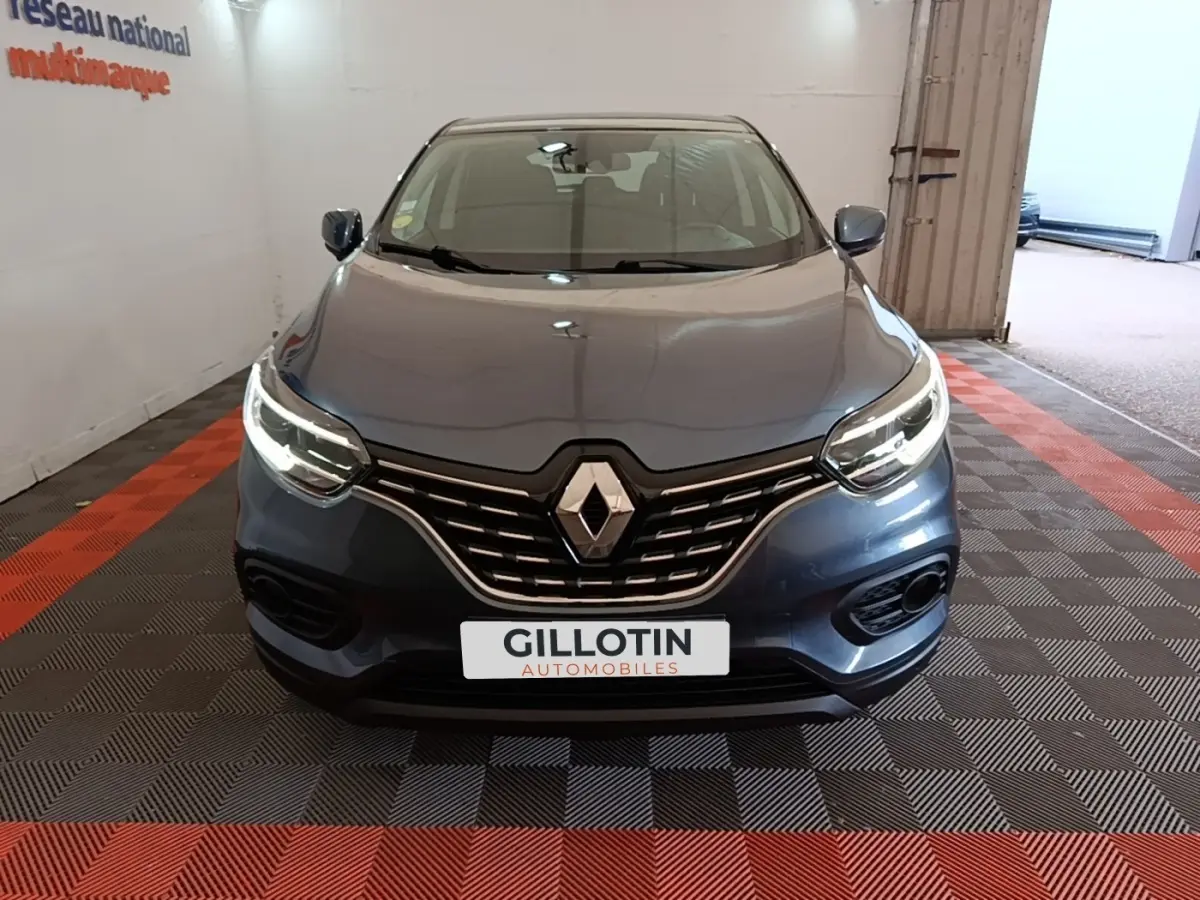 Vue frontale d'un Renault Kadjar Business gris foncé avec calandre chromée et phares LED allumés dans un showroom.