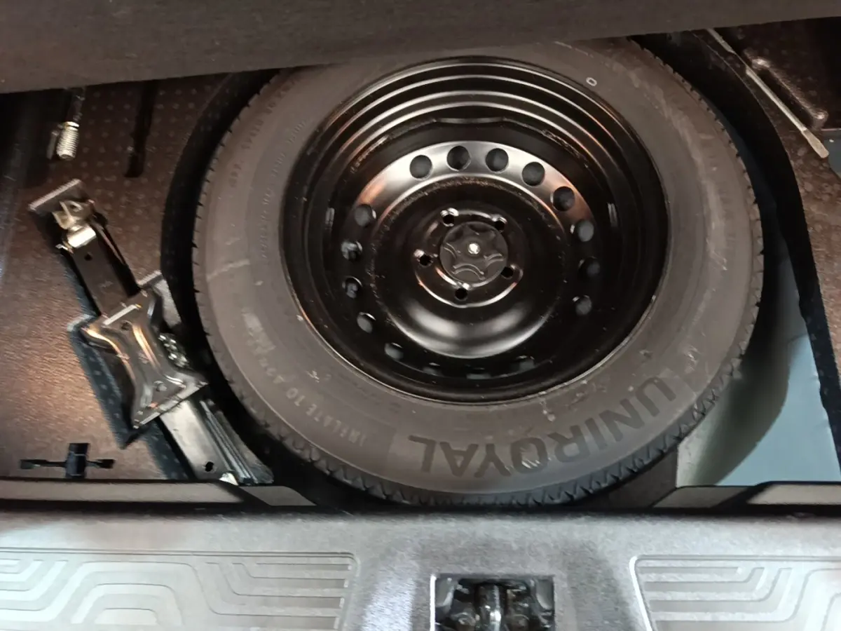 Gros plan sur la roue de secours noire et le cric dans le coffre d’un Renault Kadjar gris foncé.