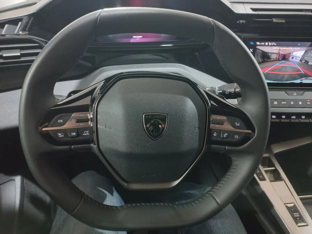 Vue rapprochée du volant cuir multifonctions Peugeot 308 PHEV 2025 avec tableau de bord numérique et écran de caméra de recul.
