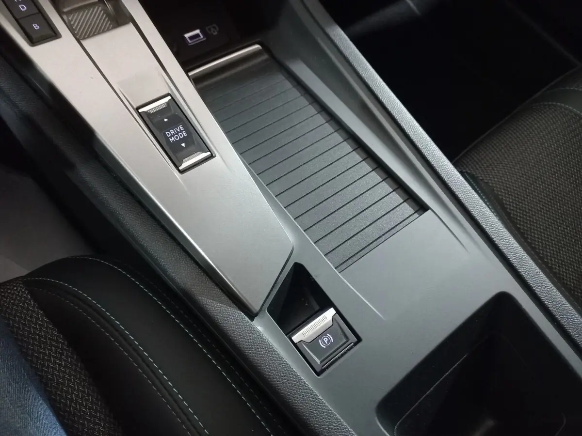 Gros plan sur la console centrale grise avec bouton Drive Mode et frein à main électrique dans Peugeot 308 PHEV 2025.
