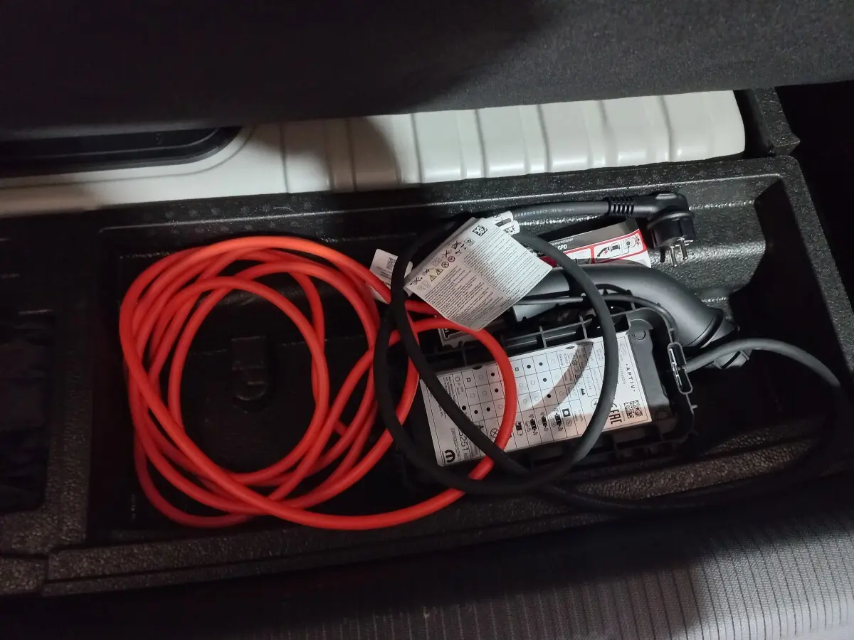 Câbles de recharge rouge et noir rangés dans le coffre d'une Peugeot 308 PHEV 180 E-EAT8 Allure gris foncé.