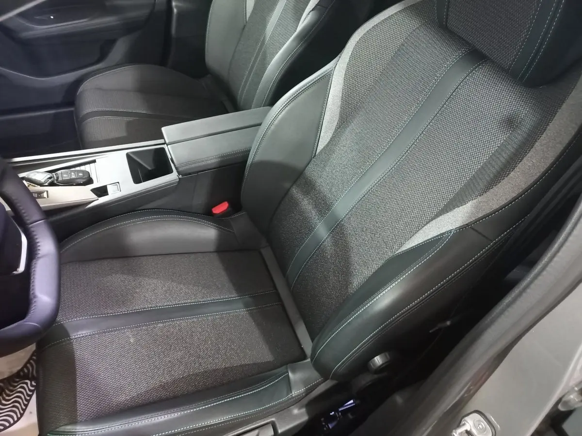 Vue intérieure côté conducteur de la Peugeot 308 PHEV 180 Allure 2025, siège tissu et cuir gris foncé avec console centrale.