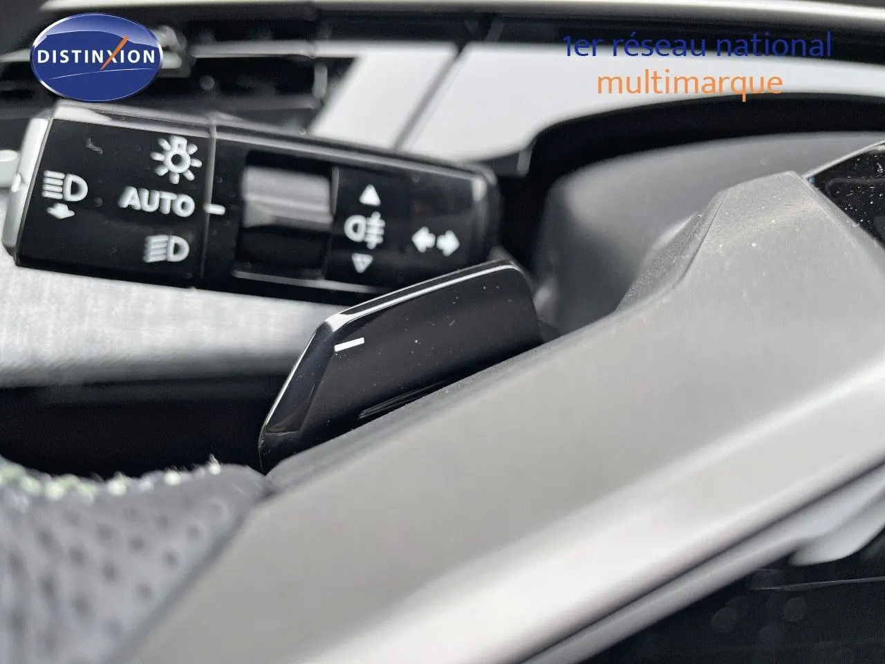 Gros plan sur la commande des feux et le volant gris clair du Peugeot 5008 Hybrid 2025, finition GT.