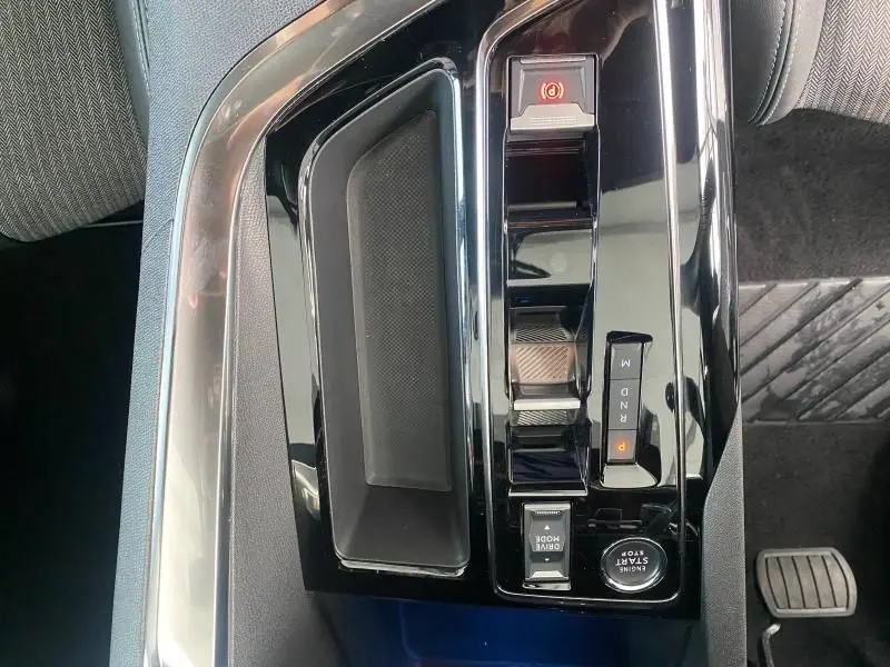 Gros plan sur la console centrale noire brillante du Peugeot 3008 2023 avec commandes de boîte auto et frein électrique.