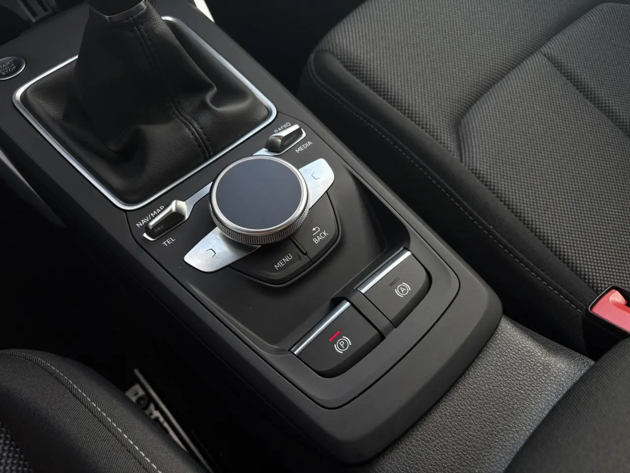 Gros plan sur la console centrale noire de l’Audi Q2 30 TFSI S-Line 2024 avec molette de commande et levier de vitesses manuel.
