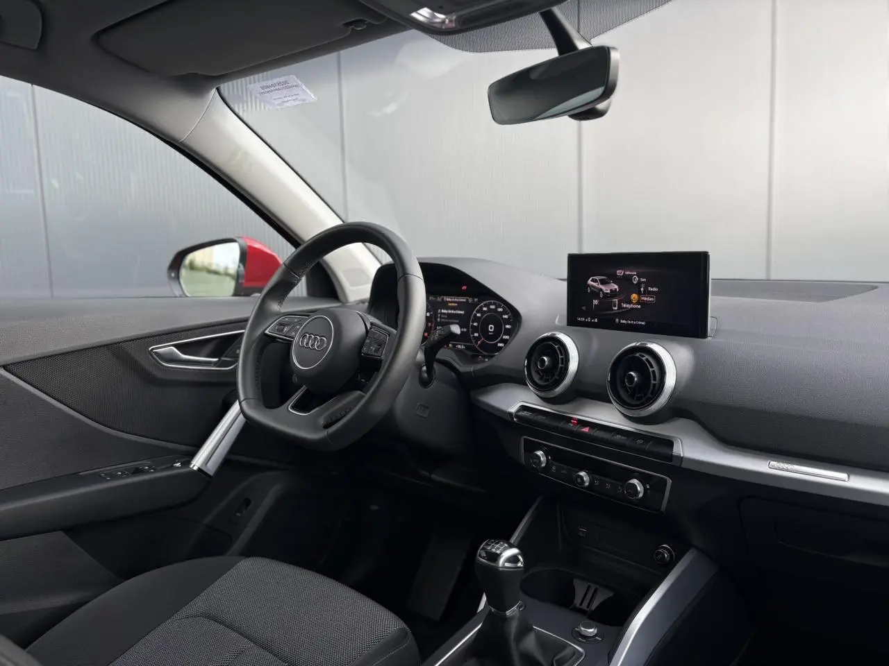 Vue intérieure côté conducteur de l'Audi Q2 30 TFSI S-Line 2024, volant cuir et écran tactile central visible.