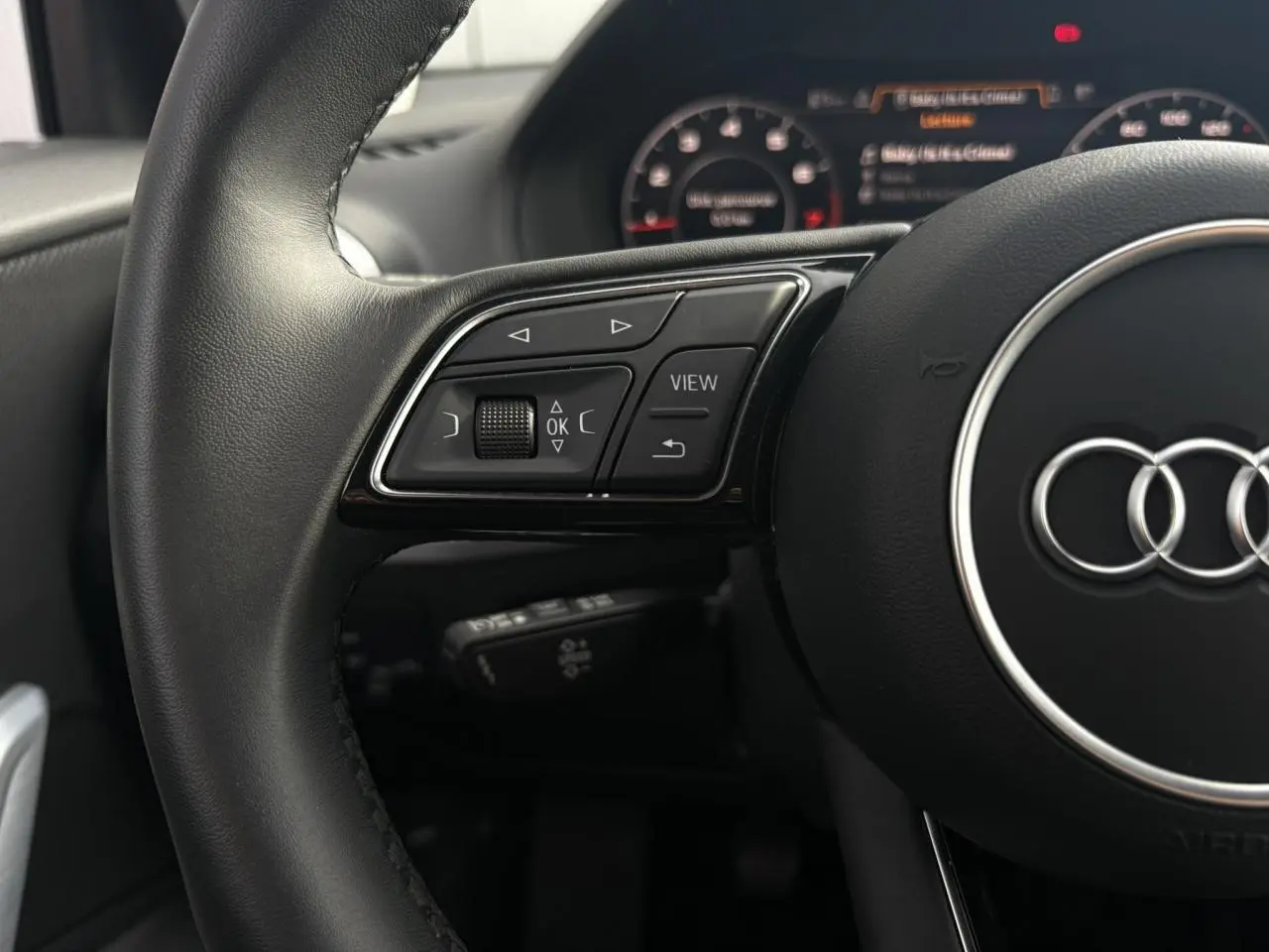 Gros plan sur le volant cuir noir de l'Audi Q2 30 TFSI S-Line 2024 avec commandes multifonctions et logo Audi central.