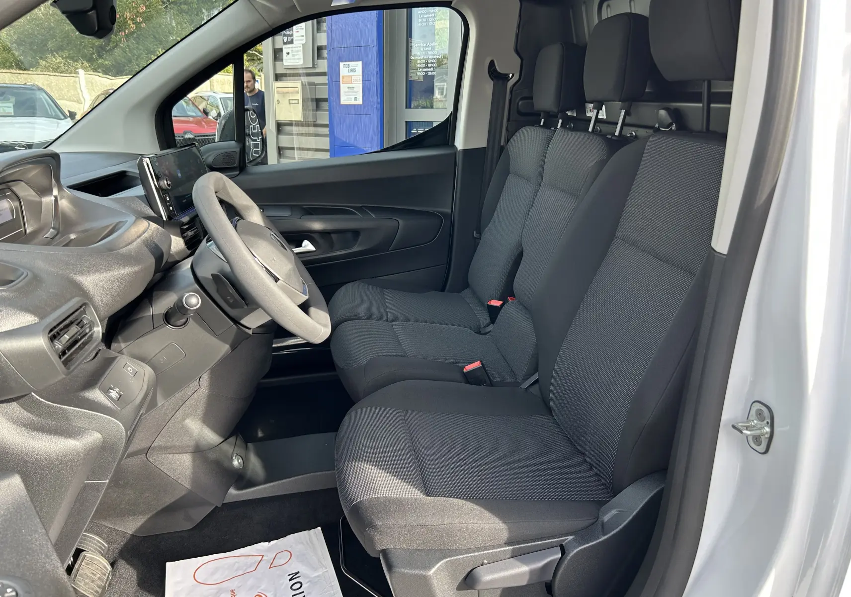 Intérieur du Peugeot Partner Fourgon blanc, vue côté conducteur montrant les sièges tissu et le tableau de bord moderne.