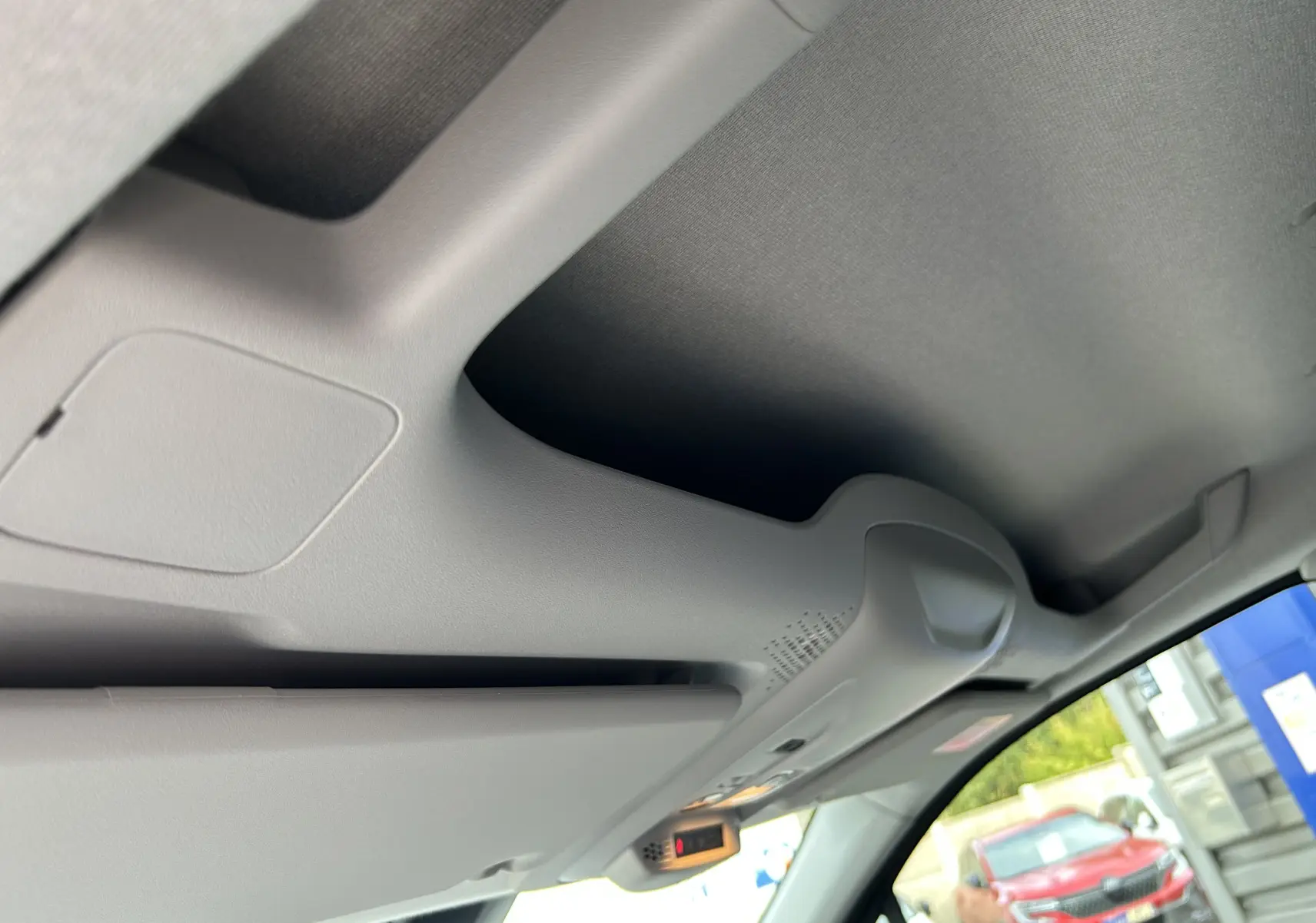 Détail du pare-soleil et plafonnier gris clair à l'intérieur du Peugeot Partner Fourgon blanc visible par la vitre côté droit.