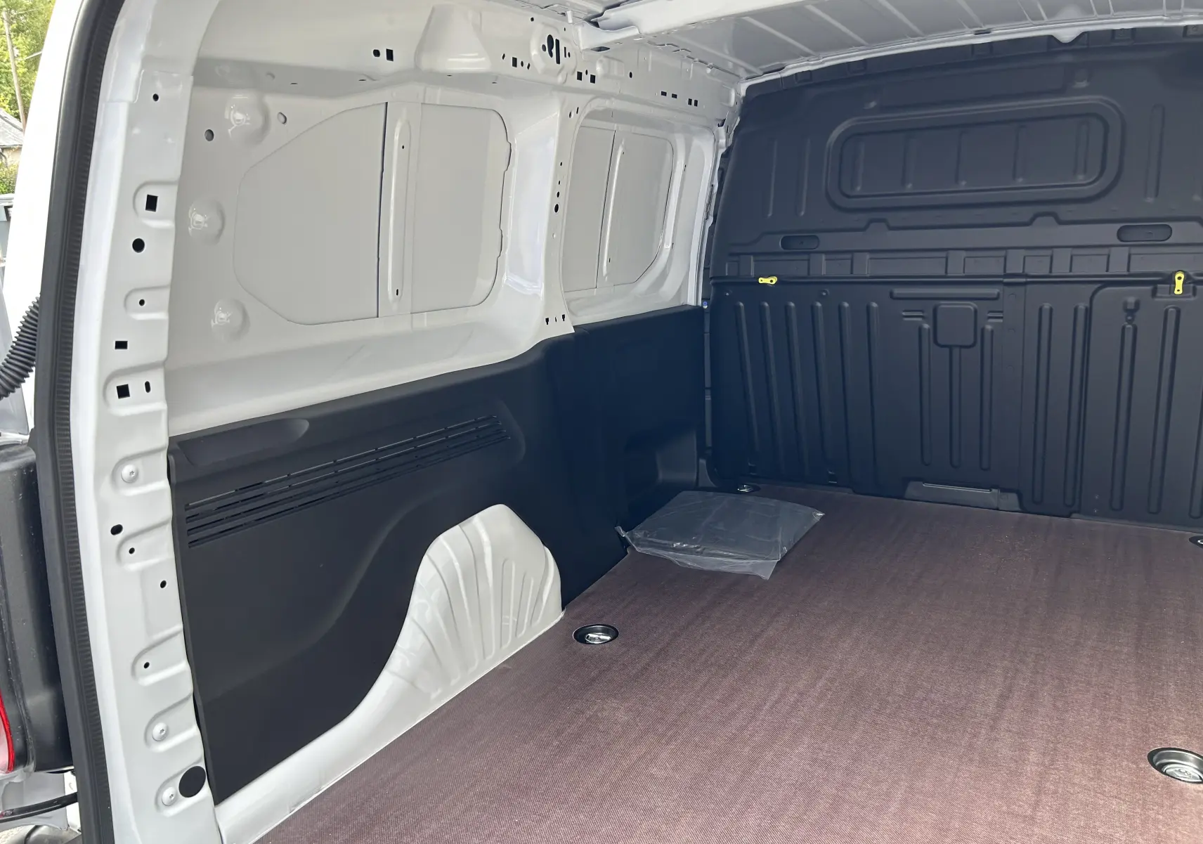 Intérieur du fourgon Peugeot Partner blanc, vue de la zone de chargement avec plancher bois et parois noires.